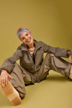 Kısa, renkli saçlı genç bir kadın yerde oturuyor, neşe ve tarz saçıyor..