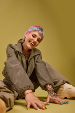 Kısa renkli saçlı genç bir kadın stüdyoda mutlu bir şekilde oturur ve oyuncu tarzını sergiler..