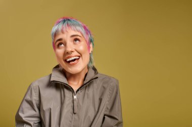 Kısa, renkli saçları olan genç bir kadın sıcak bir arka plana doğru ışıl ışıl gülümsüyor..