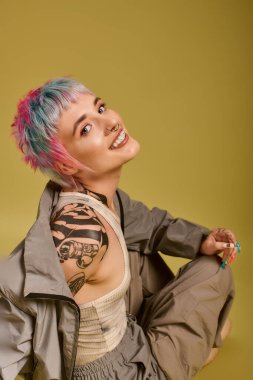 Canlı bir stüdyoda, genç bir kadın renkli saçlarını ve neşeli gülüşünü gösteriyor..