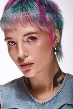 Kısa ve renkli saçlı genç bir kadın kendine güvenen bir stüdyo odasında poz veriyor..