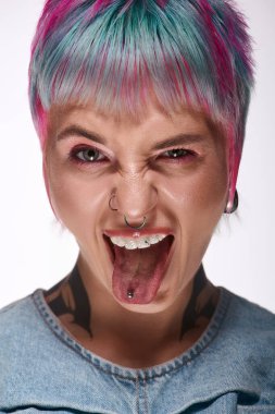 Kısa, renkli saçları olan neşeli genç bir kadın bir stüdyoda dilini şakayla uzatıyor..