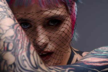 Canlı boyalı saçları olan genç bir kadın stüdyoda eşsiz stilini ve dövmelerini sergiliyor..