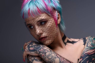 Genç bir kadın, canlı kısa saçlarını ve dövmelerini yaratıcı bir stüdyo ortamında sergiliyor..