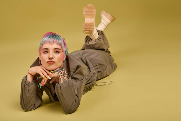 Творческая молодая женщина расслабляется на полу студии, выставляя напоказ свои красочные волосы и уникальный стиль.