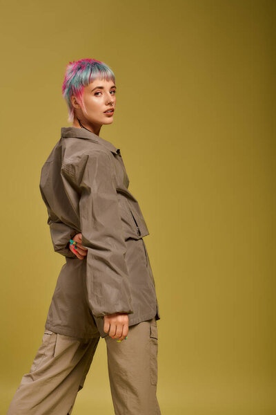 Молодая женщина стоит в студии с красочными короткими волосами, подчеркивая ее уникальное чувство моды.