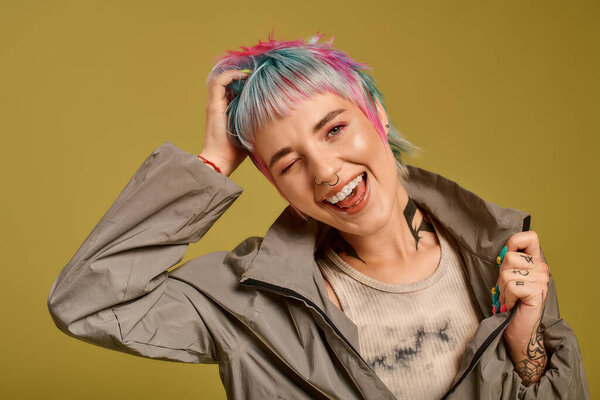 A vibrant young woman displays her colorful hair while playfully posing in a studio.
