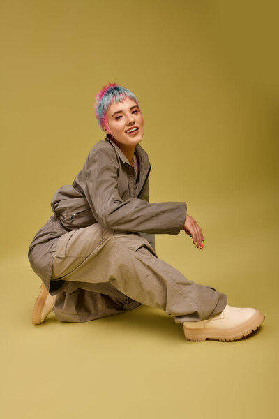 A young woman with colorful hair stylishly poses in a bright studio, showing off her fashion sense.