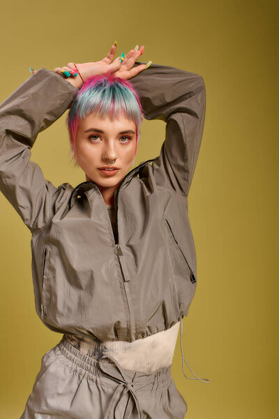 Молодая женщина уверенно позирует в студии, демонстрируя свои красочные короткие волосы и модный наряд.