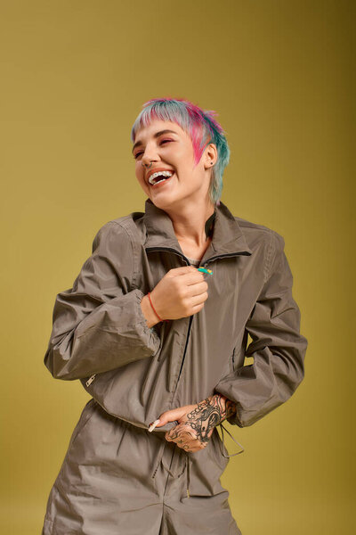 A young woman with vibrant, short hair is laughing joyfully in a studio.