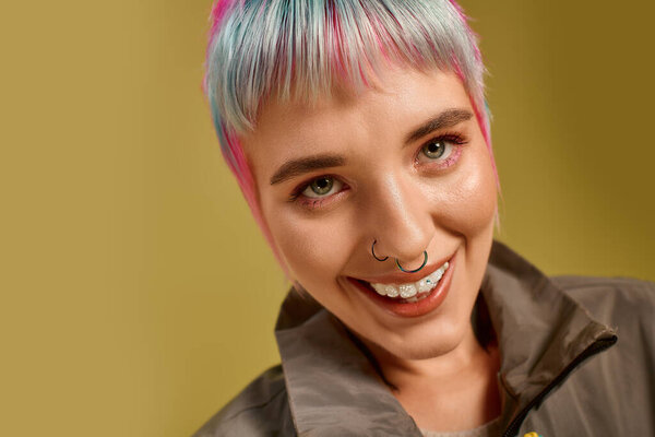A young woman with vibrant, short dyed hair shows her joy in a bright studio backdrop.