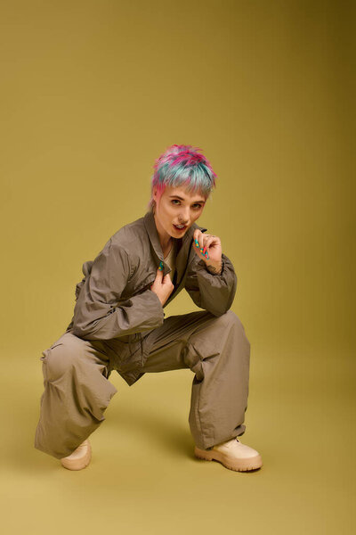 A young woman with vibrant short hair poses confidently in a studio with a unique backdrop.