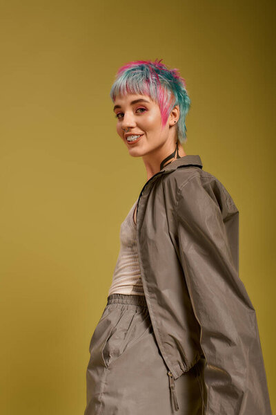 Молодая женщина с короткими, красочными волосами уверенно позирует в оживленной студии.