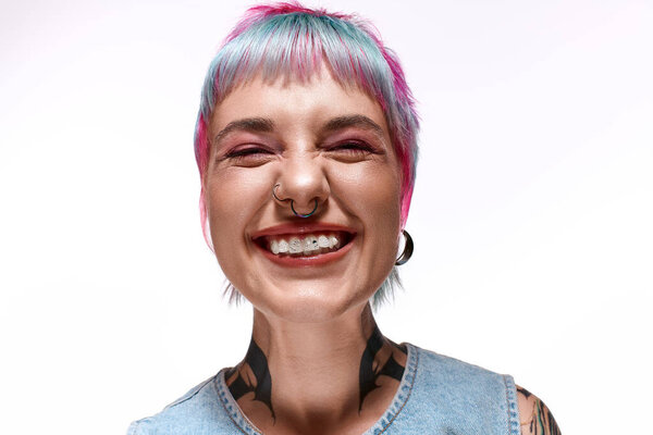 A young woman with colorful hair smiles broadly in a studio, flaunting her unique style.