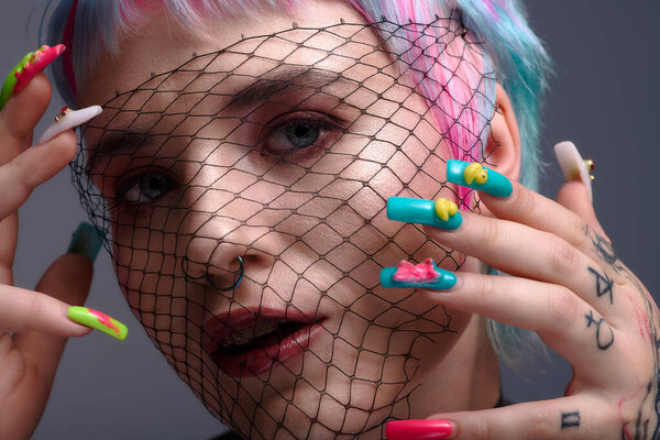 A young woman displays her unique style with short, colorful dyed hair and striking nails.