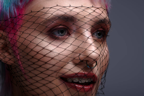 A young woman showcases her colorful short hair behind a decorative veil in a studio.