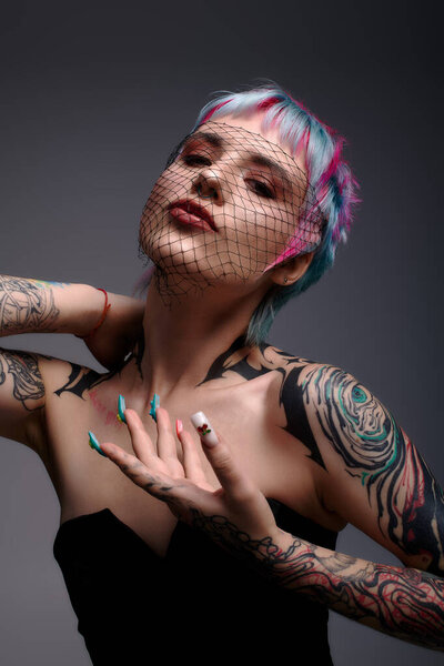 Молодая женщина с красочными короткими волосами уверенно позирует в студии, подчеркивая свой уникальный стиль.