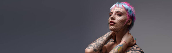 A confident young woman with short, colorful hair poses in a grey studio, banner