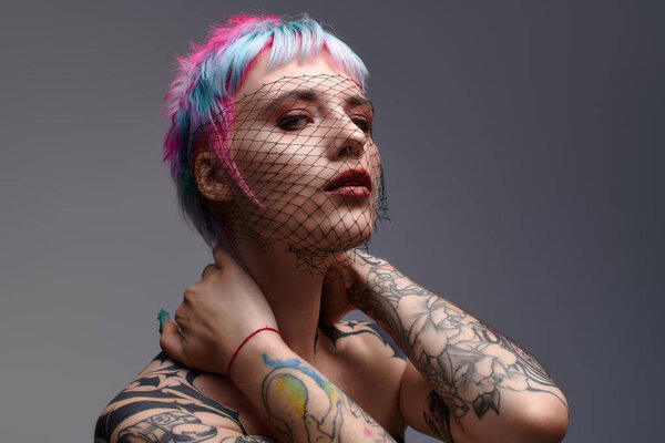 A young woman showcases her colorful short hair and tattoos in an artistic studio environment.