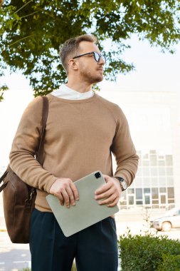 Üniversite eğitimcisi güneşli havanın tadını çıkarırken elinde tabletle dışarıda duruyor..