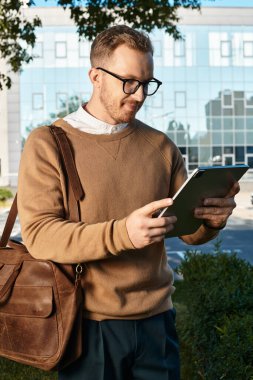 Bir adam üniversitenin dışında duruyor, tabletine dalmış, ilgisiz ve odaklanmış görünüyor..