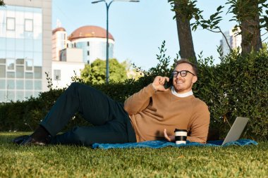 Üniversite öğretmeni yemyeşil bir alanda bir battaniyenin üzerinde gevşeyip sohbet eder..