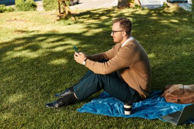 Genç bir öğretmen çimenli bir alanda dinleniyor, sıcak güneş ışığında akıllı telefonunu kontrol ediyor..