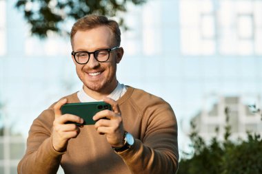 Neşeli genç bir öğretmen dışarıda akıllı telefonuyla uğraşırken gülümsüyor..