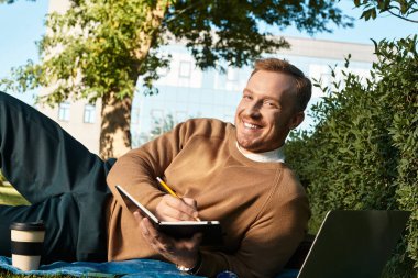 Genç bir öğretmen parkta dinlenir, güneş ışığını emerken notlar yazar..