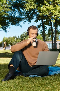 Genç bir öğretmen çimenlerde rahatlar, bilgisayarına odaklanırken kahvesini yudumlar..