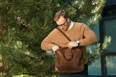 Genç bir adam, bir üniversite öğretmeni, uzun ağaçların arkasında hazırlanıyor..