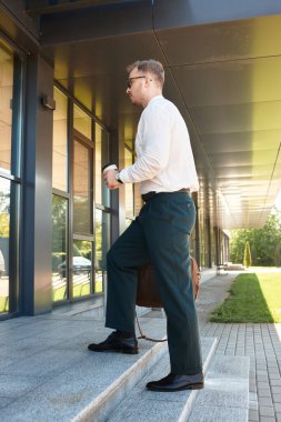 Genç erkek eğitmen elinde kahve tutarken güvenle üniversite binasına yürür..