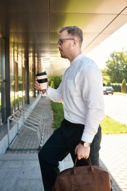 Üniversite öğretmeni elinde kahve fincanı ve çantasıyla dışarıda yürüyor. Yoğun bir gün için giyinmiş..
