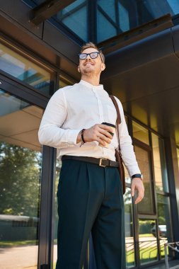 Üniversite binasının önünde elinde kahve ve kendine güvenle gülümseyen genç bir adam duruyor..