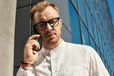 Genç bir erkek üniversite öğretmeni açık havada duruyor, açık gökyüzünün altında telefonla konuşuyor..