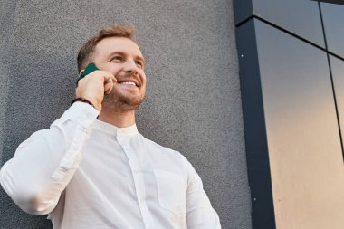 Genç bir adam, bir üniversite öğretmeni, lüks bir binanın önünde telefonuyla konuşurken gülümsüyor..