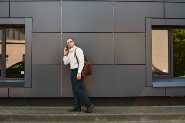 Profesyonel kıyafetli genç adam çağdaş bir binanın önünde yürüyor ve konuşuyor..