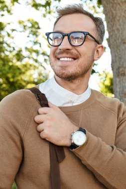 Sıradan giyinmiş genç bir adam yemyeşil bir ortamda poz verirken neşe sergiliyor..