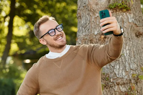 Genç bir adam, bir üniversite öğretmeni, doğada selfie çekerken ışıl ışıl gülümser..