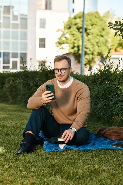 Genç bir erkek öğretmen güneşli bir günde yeşil çimenlikteki bir battaniyeye oturup dinlenir..