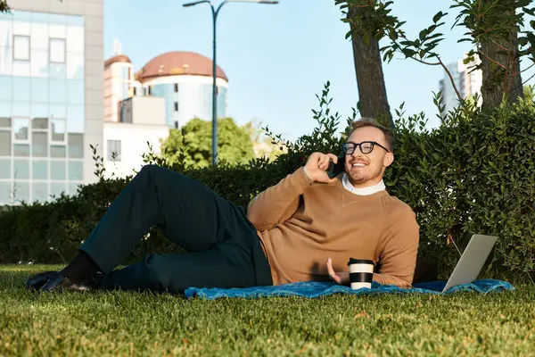 Üniversite öğretmeni yemyeşil bir alanda bir battaniyenin üzerinde gevşeyip sohbet eder..