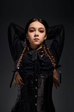 Gotik tarzı bir kostüm giymiş, örgülü genç bir kız çarşamba karakteriyle hava atıyor..