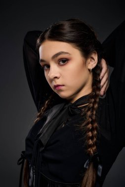 Gotik çarşamba kostümü giymiş bir çocuk saçlarını örerek dramatik bir şekilde poz verir..