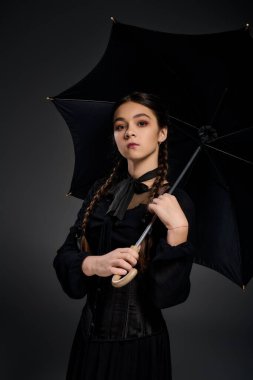Gotik çarşamba kıyafetli bir kız elinde cadılar bayramı için hazır siyah bir şemsiye tutuyor..