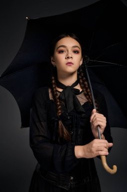 Gotik tarzı çarşamba kostümü giymiş bir kız ürkütücü sezonda elinde şemsiyeyle dikiliyor..