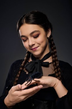 Çarşamba günü gotik bir kıyafet giymiş bir kız elinde ürkütücü bir örümceği tutarken gülümsüyor..