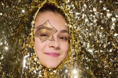 Yüzünde yıldız olan sevimli bir kız. Cadılar Bayramı boyunca altın pullarla çevrili..