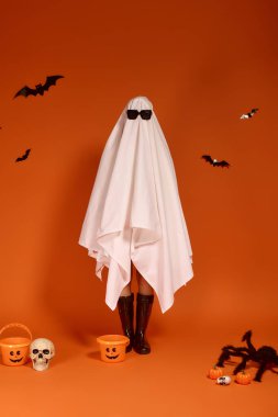 Hayalet kostümlü bir çocuk, cadılar bayramını turuncu bir arka planda neşeyle kutluyor..