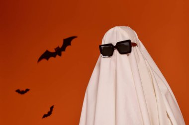 Çocukken Cadılar Bayramı kutlaması turuncu bir fonda hayalet kostümü giyer..