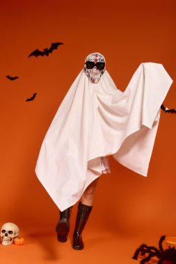 Hayalet kostümlü bir çocuk, turuncu bir arka planda Cadılar Bayramı 'nı neşeyle kutluyor..